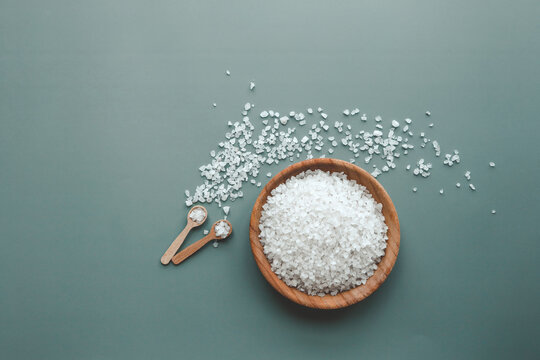 White sea salt in wooden plate on green background, home spa - Powered by Adobe