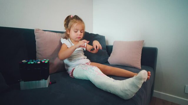 Child Is Alone. Loneliness Due To Illness. A Girl With A Broken Leg Is Sad And Draws On A Bandage.