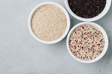 Quinoa mixed. Red black white quinoa seeds in bowls on gray stone background, top view.