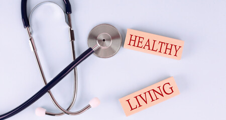 On a blue background, a stethoscope and wooden block with the word HEALTHY LIVING .Medical concept