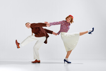 Young man and woman in stylish clothes expressively dancing retro dance against grey studio...