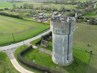 Drone view of a concrete water tower which has an array of 5G antennas on its circular roof....