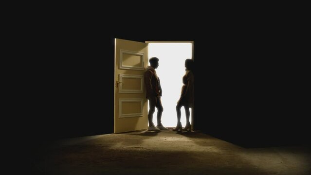 Side view of couple standing opposite and looking each other in front of an open door with white light behind . Footage of couple stand on floor behind stars.  Concept of dream or romance. Slow Motion