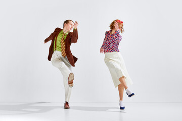 Young man and woman in stylish bright colorful clothes dancing retro dance against grey studio...