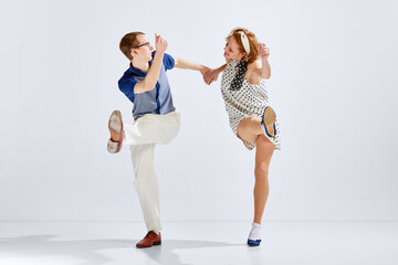 Beautiful young couple, man and woman in stylish retro costumes dancing dance against grey studio...