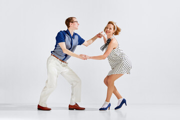 Young man and woman in stylish clothes dancing retro dance against grey studio background. Social...