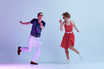 Beautiful young couple, man and woman in stylish costumes dancing retro dances against gradient...