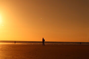 Fototapeta na wymiar Ambient orange sunset on beach with silhouette of man