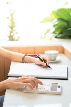 Close up working women hand using caculator caculate financial and note on paper with favorite cup of coffee hot latte. Business and financial concept. caculator on the table.