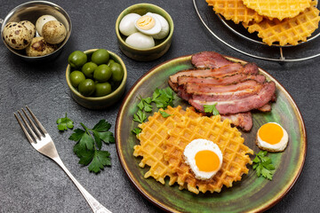 Quail eggs and green olives in bowls. Fried bacon, waffles and eggs in a frying pan.