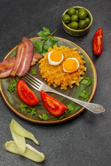 Two slices of tomato, waffles, fried bacon and two eggs, a fork on a plate.