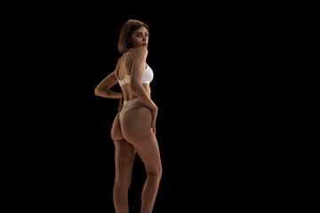 Naklejka premium Charming girl with blonde hair. Portrait of young slim beautiful girl wearing white underwear posing over black background.