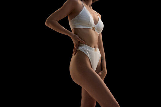 Cropped image. Young slim sensual woman wearing white inner wear posing over dark background.
