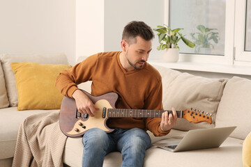 Man learning to play guitar with online music course at home. Time for hobby