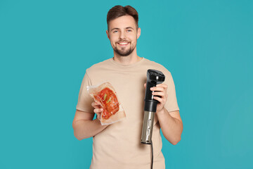 Smiling man holding sous vide cooker and meat in vacuum pack on light blue background