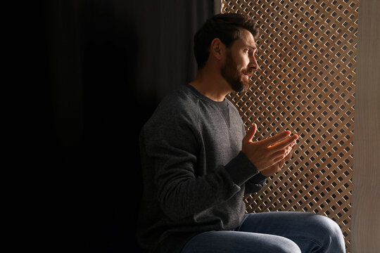Man listening to priest during confession in booth, space for text