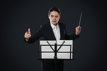 Professional conductor with baton and note stand on dark background