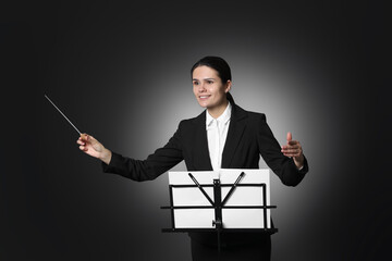 Happy professional conductor with baton and note stand on black background