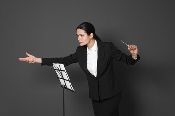 Happy professional conductor with baton and note stand on grey background © New Africa