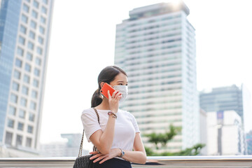 Young adult asian business single woman talking with smart phone. Wearing face mask new normal lifestyles. City lifestyle working people. Backgroud at outdside on day.