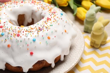 Easter cake with sprinkles, decorative bunnies and tulips on wooden table