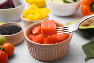 Holding salmon on fork at white table, closeup. Preparing poke bowl
