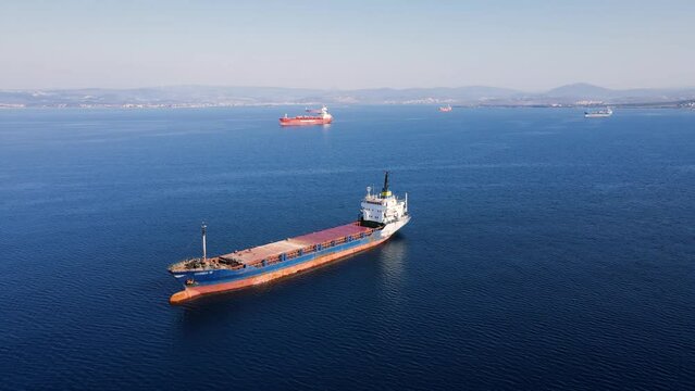 General cargo ship or bulk carrier anchored at sea nearby port awaiting loading, Aerial establishing shot