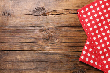 Red checkered tablecloth on wooden table, top view. Space for text