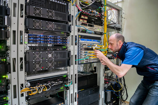 A man commutes wires in a server room. A technician works with server equipment in a data center.