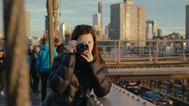 Cute girl taking photos with camera on a Brooklyn bridge at sunset, New York