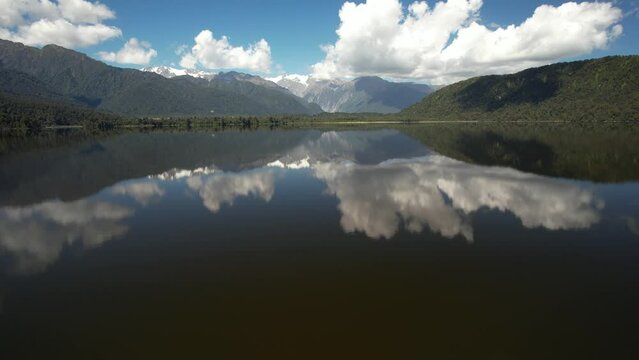 Drone fly over mirror water surface, reflection of mountain vista and natural scenery. Lake Mapourika, New Zealand
