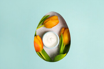?osmetics cream with yellow tulips in an easter egg. blue background with copy space
