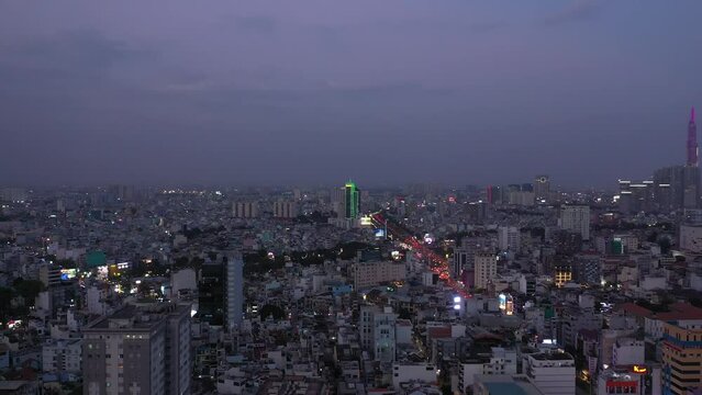 Ho Chi Minh City, Vietnam evening featuring canal, landmark building and view over rooftops to urban sprawl and main road under lights. Aerial crane shot