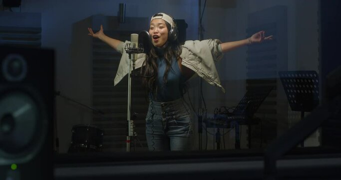 Portrait of a Professional Female Asian Singer Recording a Song in a Studio. Beautiful Young Artist Enjoying Performing her New Single, Singing Energetically with an Expressive Face and Gestures