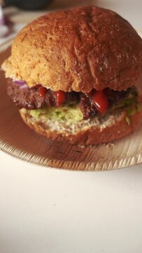 Hamburger brown bun sandwich with avocado, ketchup and red onion, vertical 4k shot