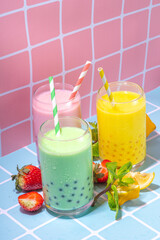 Set of three colorful summer bubble tea, bright creamy pearl tea or latte tapioca drinks, pink berry, yellow citrus, green mint, with tapioca balls and crushed ice, on colorful tile background