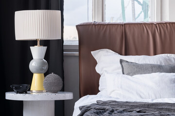 Elegant lamp on bedside table next to cozy bed