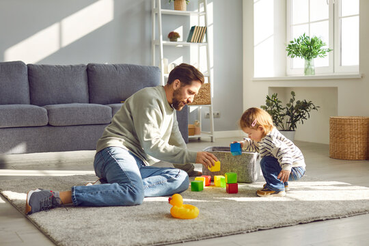 Parenthood. Loving young father with his toddler daughter playing with colored blocks at home. Caucasian father sitting on floor in living room enjoy leisure weekend together with his small child. - Powered by Adobe