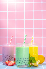 Set of three colorful summer bubble tea, bright creamy pearl tea or latte tapioca drinks, pink berry, yellow citrus, green mint, with tapioca balls and crushed ice, on colorful tile background
