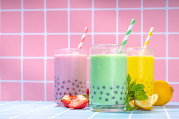 Set of three colorful summer bubble tea, bright creamy pearl tea or latte tapioca drinks, pink berry, yellow citrus, green mint, with tapioca balls and crushed ice, on colorful tile background