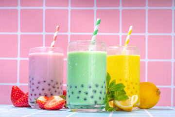 Set of three colorful summer bubble tea, bright creamy pearl tea or latte tapioca drinks, pink berry, yellow citrus, green mint, with tapioca balls and crushed ice, on colorful tile background