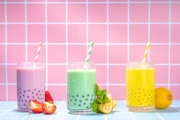 Fototapeta premium Set of three colorful summer bubble tea, bright creamy pearl tea or latte tapioca drinks, pink berry, yellow citrus, green mint, with tapioca balls and crushed ice, on colorful tile background