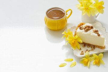 cheesecake with cup of tea and yellow spring flowers on white table