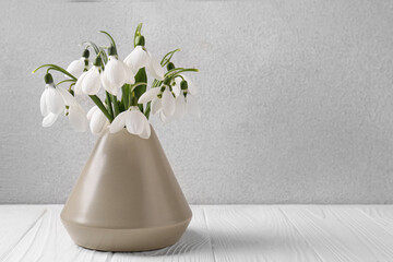 Beautiful snowdrops in vase on white wooden table, space for text