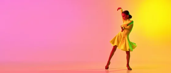 Fotobehang Dansschool Elegant little girl in adorable stage outfit, dress dancing ballroom dance over gradient pink-yellow background in neon light filter. Concept of beauty, professional dances, skills