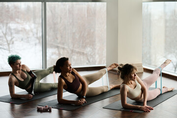 Young healthy women lying on exercise mat and exercising with rubber band during sport training in...