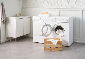 White bathroom, washing and dry machine, brick wall and transparent screen, cabinet sink and mirror, plant, dirty laundry.