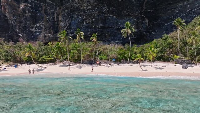 Aerial trucking shot of tourist resting on PLAYA FRONTON in front of steep mountain,Dominican Republic