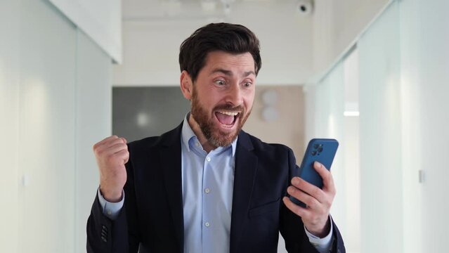 Successful businessman looks at momile phone in the office lobby with a look of amazement on his face. Man just received some good news related to finance or his salary. Won lottery or a big contract.