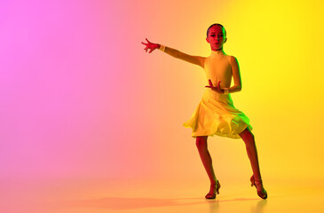 Fototapeta na wymiar Expressive little girl in adorable stage outfit, dress dancing ballroom dance over gradient pink-yellow background in neon light filter. Concept of beauty, professional dances, skills